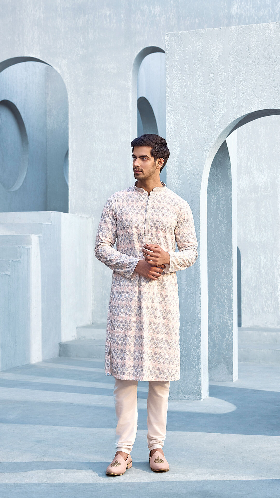 Man wearing a pastel printed kurta with churidar, standing in a modern architectural setting, showcasing elegant traditional Indian menswear